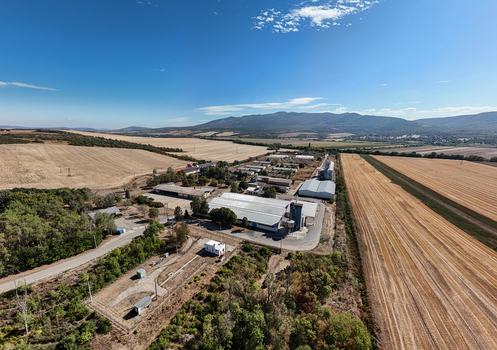 Aerial view of farmland and agricultural buildings with silos near Paszto Hungary surrounded by wheat fields roads forest edges and hills under a clear sky. Aerial view of farmland and agricultural buildings with silos near Paszto Hungary surrounded by wheat fields roads forest edges and hills under a clear sky.