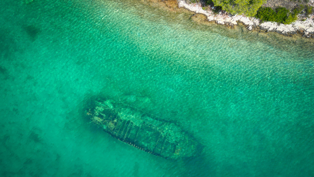 Aerial view of the submerged Kontesa shipwreck in the crystal clear turquoise waters of the bay near the rocky shoreline in Necujam Split Dalmatia County Croatia. Aerial view of the submerged Kontesa shipwreck in the crystal clear turquoise waters of the bay near the rocky shoreline in Necujam Split Dalmatia County Croatia.