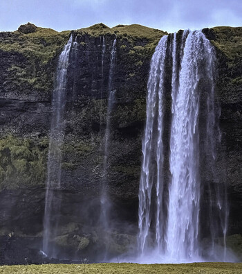 View of the cascading Seljalandsfoss waterfall plunging over a rugged cliff face with mossy green slopes and misty water spray in Seljalandsfoss Iceland. View of the cascading Seljalandsfoss waterfall plunging over a rugged cliff face with mossy green slopes and misty water spray in Seljalandsfoss Iceland.