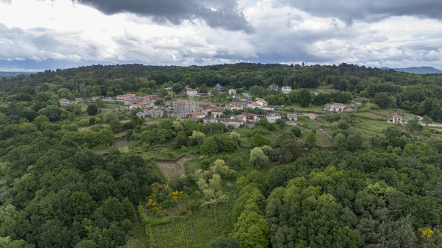 Aerial view of the Iglesia de Santa Marina de Augas Santas and the historic village surrounded by lush green forests under a cloudy sky in Augas Santas Ourense Spain. Aerial view of the Iglesia de Santa Marina de Augas Santas and the historic village surrounded by lush green forests under a cloudy sky in Augas Santas Ourense Spain.