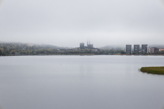 View of a calm lake with industrial buildings and residential towers partially obscured by thick morning fog in Jyvaskyla Central Finland Finland.
