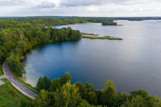 Aerial view of a vast blue lake surrounded by lush green forests and a winding road under a cloudy sky in Lithuania. Aerial view of a vast blue lake surrounded by lush green forests and a winding road under a cloudy sky in Lithuania.