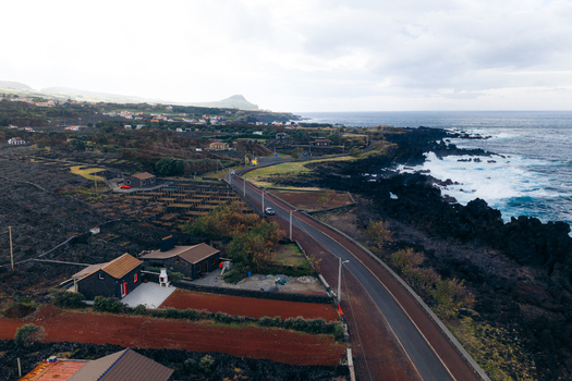 Aerial view of a coastal road winding through volcanic rock formations and traditional vineyards along the rocky shoreline in Biscoitos Azores Portugal. Aerial view of a coastal road winding through volcanic rock formations and traditional vineyards along the rocky shoreline in Biscoitos Azores Portugal.