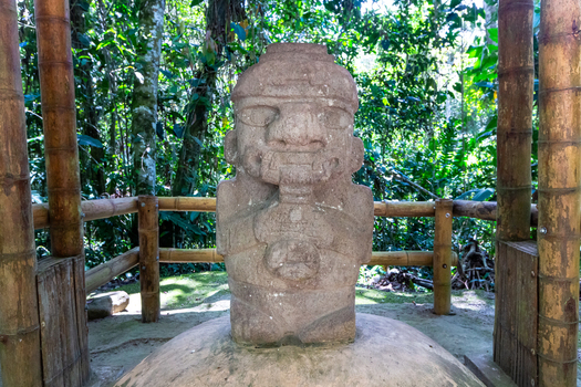 View of a pre Columbian stone statue at San Agustin Archaeological Park surrounded by a bamboo fence and lush forest vegetation in San Agustin Huila Colombia.