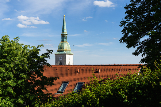 View of the green spire of St. Martin s Cathedral rising above red tiled rooftops and lush green trees under a blue sky Bratislava Bratislava Region Slovakia. View of the green spire of St. Martin s Cathedral rising above red tiled rooftops and lush green trees under a blue sky Bratislava Bratislava Region Slovakia.
