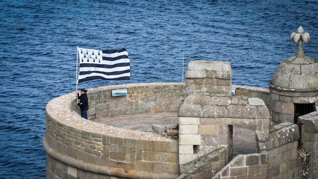 Aerial view of a Bretagne flag waving strongly from a stone tower of Chateau du Taureau overlooking the deep blue sea Plouezoc h Bretagne France. Aerial view of a Bretagne flag waving strongly from a stone tower of Chateau du Taureau overlooking the deep blue sea Plouezoc h Bretagne France.