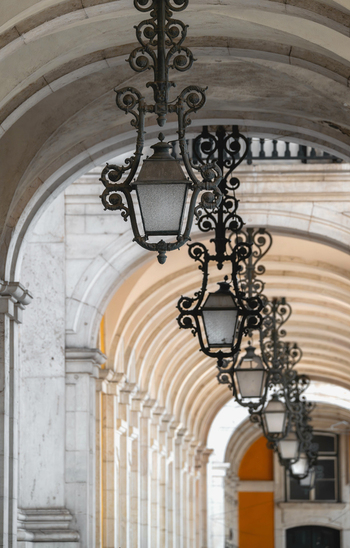 View of ornate wrought iron lanterns hanging from the vaulted stone arches of the Praca do Comercio colonnade in Lisbon Lisbon Portugal.