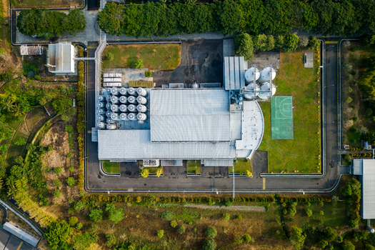 Aerial view of an industrial factory complex with storage silos a large warehouse and a small sports court surrounded by trees in Semarang Regency Central Java Indonesia. Aerial view of an industrial factory complex with storage silos a large warehouse and a small sports court surrounded by trees in Semarang Regency Central Java Indonesia.