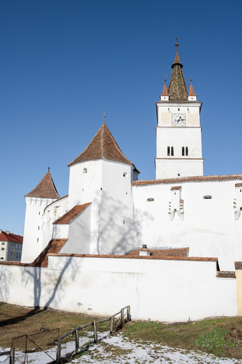 View of the historic Prejmer Fortified Church with its white defensive walls clock tower and red tiled roofs under a clear blue sky in Prejmer Brasov Romania. View of the historic Prejmer Fortified Church with its white defensive walls clock tower and red tiled roofs under a clear blue sky in Prejmer Brasov Romania.