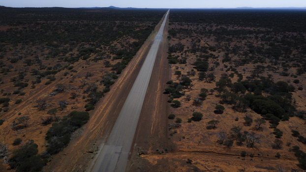 Aerial view of a long straight asphalt road stretching through the vast arid outback landscape with sparse vegetation and red earth in Perth Western Australia Australia.