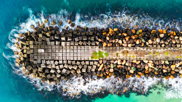 Aerial view of The Spit Gold Coast breakwater featuring concrete tetrapods and stone blocks surrounded by turquoise ocean waves in Main Beach Queensland Australia.