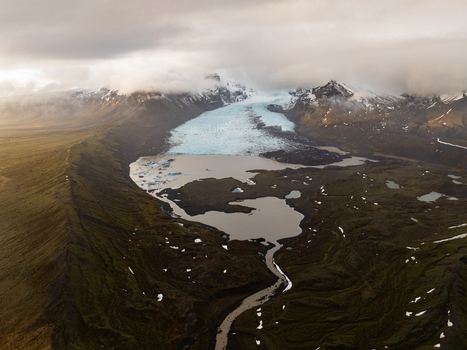 Aerial view of Kviarjokull glacier flowing into a glacial lagoon surrounded by mossy mountains and clouds in Hornafjordur Iceland.