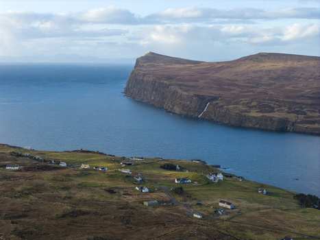 Aerial view of the coastal village of Milovaig with scattered white houses on green hills overlooking the blue sea and dramatic cliffs Milovaig Scotland United Kingdom.