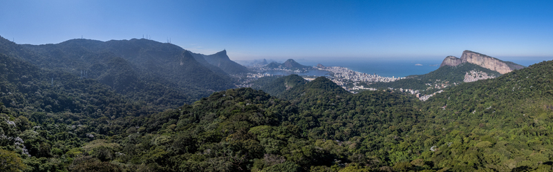 Aerial view of Tijuca National Park featuring dense tropical forest rugged mountain peaks and the distant urban skyline of Rio de Janeiro Rio de Janeiro Brazil.