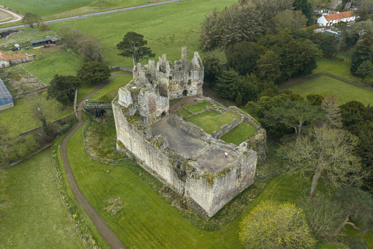 Aerial view of the historic ruins of Dirleton Castle and Gardens surrounded by lush green lawns and dense trees in Dirleton Scotland United Kingdom. Aerial view of the historic ruins of Dirleton Castle and Gardens surrounded by lush green lawns and dense trees in Dirleton Scotland United Kingdom.