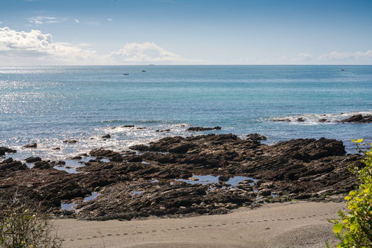 View of the rocky coastline along the South West Coastal Path overlooking Portnadler Bay with calm blue sea and clear sky in Looe Cornwall United Kingdom. View of the rocky coastline along the South West Coastal Path overlooking Portnadler Bay with calm blue sea and clear sky in Looe Cornwall United Kingdom.
