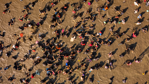 Aerial view of a large crowd of people gathered in a muddy field many holding fishing nets and participating in a communal activity in Kalikotes Central Java Indonesia.