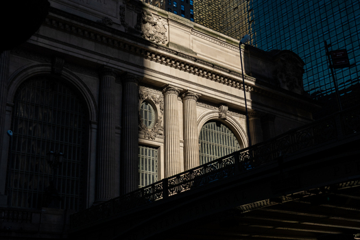 View of the neoclassical facade of Grand Central Terminal with stone columns and arched windows under dramatic shadows in New York New York United States. View of the neoclassical facade of Grand Central Terminal with stone columns and arched windows under dramatic shadows in New York New York United States.