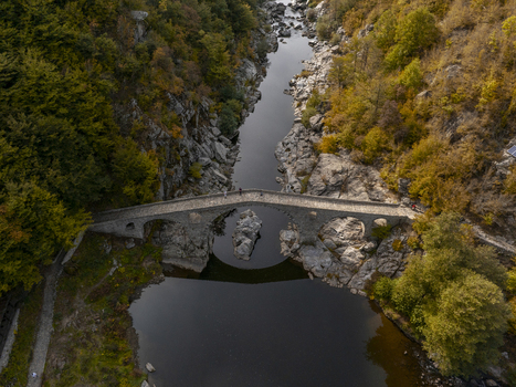 Aerial view of the historic stone Devil s bridge spanning the Arda river in a deep rocky gorge surrounded by vibrant autumn forest in Kardzhali Province Bulgaria. Aerial view of the historic stone Devil s bridge spanning the Arda river in a deep rocky gorge surrounded by vibrant autumn forest in Kardzhali Province Bulgaria.