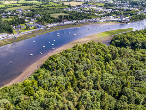 Aerial view of the River Moy flowing past the town of Ballina with small boats moored in the water surrounded by lush green forests and residential areas in Ballina County Mayo Ireland.
