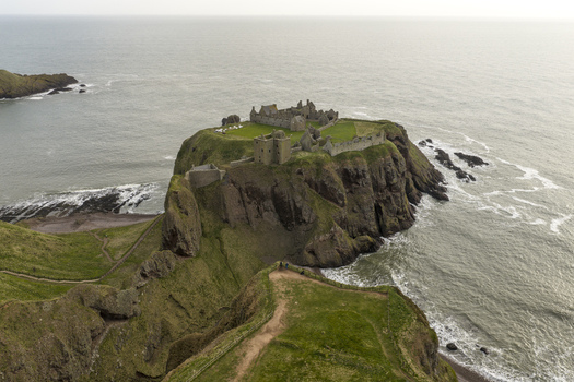 Aerial view of Dunnottar Castle a medieval fortress perched on a dramatic rocky headland surrounded by the North Sea and green cliffs in Stonehaven Scotland United Kingdom. Aerial view of Dunnottar Castle a medieval fortress perched on a dramatic rocky headland surrounded by the North Sea and green cliffs in Stonehaven Scotland United Kingdom.
