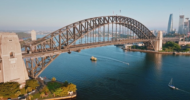 Aerial view of the Sydney Harbour Bridge spanning the harbour with a ferry and sailboat below surrounded by the city skyline in Sydney New South Wales Australia. Aerial view of the Sydney Harbour Bridge spanning the harbour with a ferry and sailboat below surrounded by the city skyline in Sydney New South Wales Australia.