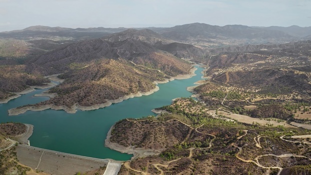 Aerial view of a reservoir and dam surrounded by arid mountains winding dirt roads and sparse vegetation in Cyprus. Aerial view of a reservoir and dam surrounded by arid mountains winding dirt roads and sparse vegetation in Cyprus.