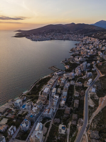 Aerial view of the coastal city of Saranda at sunset featuring residential buildings a winding road along the coastline and the Ionian Sea in Saranda Vlore County Albania. Aerial view of the coastal city of Saranda at sunset featuring residential buildings a winding road along the coastline and the Ionian Sea in Saranda Vlore County Albania.