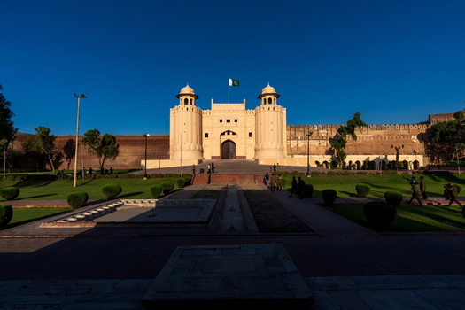 View of the historic Lahore Fort with its iconic Alamgiri Gate stone walls and surrounding green gardens under a clear blue sky in Lahore Punjab Pakistan.