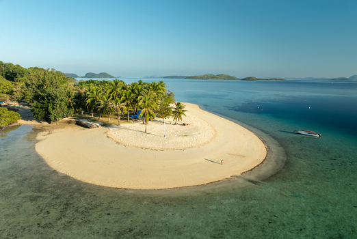 Aerial view of Pass Island with its white sand beach lush palm trees and turquoise waters under a clear blue sky in Coron Philippines. Aerial view of Pass Island with its white sand beach lush palm trees and turquoise waters under a clear blue sky in Coron Philippines.