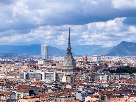 Aerial view of the Mole Antonelliana towering over the historic rooftops and urban skyline with mountains under a cloudy sky in Turin Piedmont Italy. Aerial view of the Mole Antonelliana towering over the historic rooftops and urban skyline with mountains under a cloudy sky in Turin Piedmont Italy.