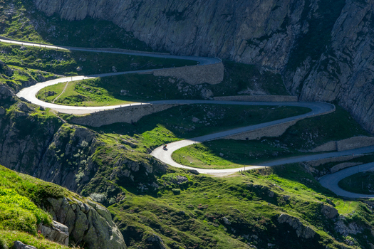 View of the winding Tremola road at Sankt Gotthard Pass with hairpin turns carved into the rocky mountain slopes under bright sunlight in Airolo Ticino Switzerland.