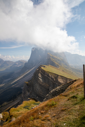 View of the sharp mountain ridges and green alpine meadows of the Dolomites under a cloudy blue sky in Rocca Pietore Veneto Italy. View of the sharp mountain ridges and green alpine meadows of the Dolomites under a cloudy blue sky in Rocca Pietore Veneto Italy.