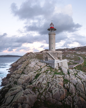 Aerial view of the Faro de Punta Nariga lighthouse standing on rugged granite cliffs overlooking the Atlantic Ocean under a cloudy twilight sky Malpica A Coruna Spain. Aerial view of the Faro de Punta Nariga lighthouse standing on rugged granite cliffs overlooking the Atlantic Ocean under a cloudy twilight sky Malpica A Coruna Spain.