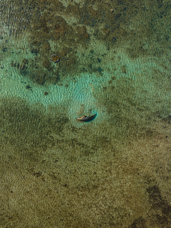 Aerial view of a lone shipwreck lies in clear turquoise waters revealing the intricate patterns of the seabed below Goro South Province New Caledonia. Aerial view of a lone shipwreck lies in clear turquoise waters revealing the intricate patterns of the seabed below Goro South Province New Caledonia.