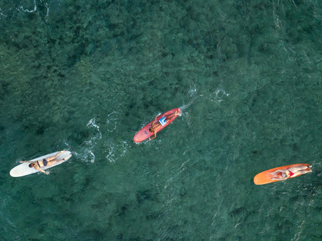 Aerial view of people on surfboards floating on the clear turquoise water at Mahaybo Beach in General Luna Caraga Philippines. Aerial view of people on surfboards floating on the clear turquoise water at Mahaybo Beach in General Luna Caraga Philippines.