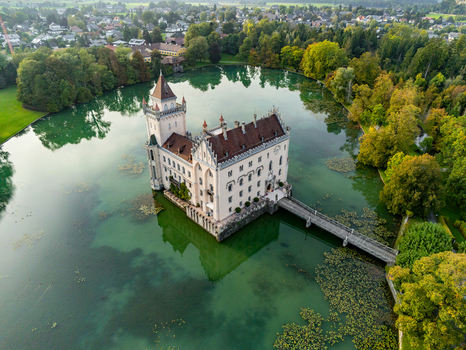 Aerial view of Schloss Anif a historic water castle surrounded by a lush green lake dense trees and a wooden bridge in Anif Salzburg Austria.