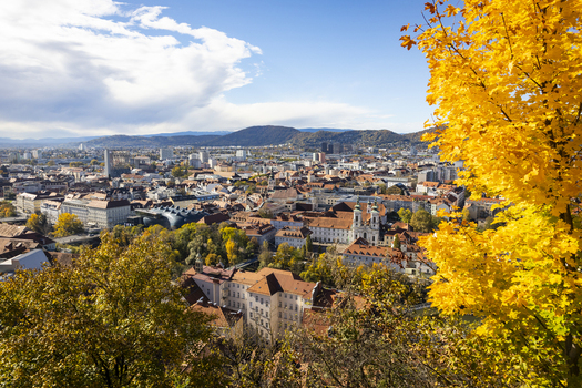 View of the city unfolds beneath a canopy of golden autumn leaves buildings huddle together amidst rolling hills under a bright sky Graz Styria Austria. View of the city unfolds beneath a canopy of golden autumn leaves buildings huddle together amidst rolling hills under a bright sky Graz Styria Austria.