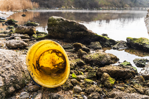 View of a yellow plastic bucket abandoned on the rocky and mossy shoreline of Lake Varna Varna Bulgaria. View of a yellow plastic bucket abandoned on the rocky and mossy shoreline of Lake Varna Varna Bulgaria.