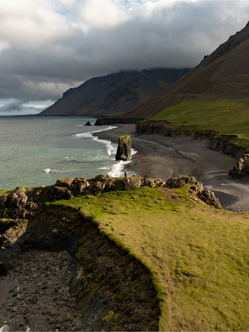 Aerial view of the dramatic Stapavik coastline featuring a black sand beach rugged cliffs and lush green grass in Njardhvik Mulathing Iceland. Aerial view of the dramatic Stapavik coastline featuring a black sand beach rugged cliffs and lush green grass in Njardhvik Mulathing Iceland.
