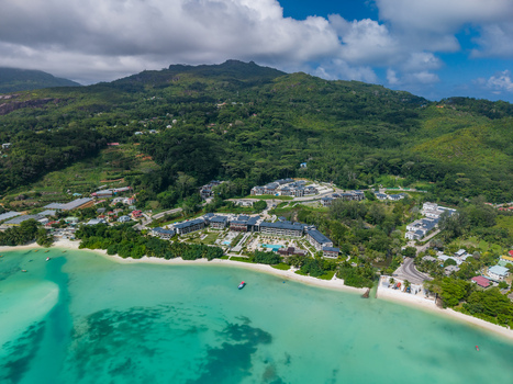 Aerial view of turquoise waters meet the shore buildings nestled amongst lush greenery against a backdrop of rolling mountains Victoria Mahe Island Seychelles. Aerial view of turquoise waters meet the shore buildings nestled amongst lush greenery against a backdrop of rolling mountains Victoria Mahe Island Seychelles.