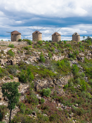 Aerial view of Moinhos da Serra da Atalhada with traditional stone windmills situated on a rocky hillside covered with green vegetation under a cloudy sky in Penacova Coimbra Portugal.
