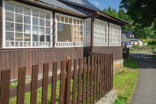 View of rustic charm with a dark wooden house featuring bright white framed windows and a quaint brown fence along a paved path Donovaly Banskobystricky kraj Slovakia. View of rustic charm with a dark wooden house featuring bright white framed windows and a quaint brown fence along a paved path Donovaly Banskobystricky kraj Slovakia.