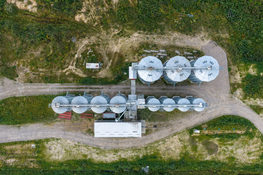 Aerial view of a grain storage facility with rows of circular metal silos surrounded by rural fields and gravel paths in Poland.