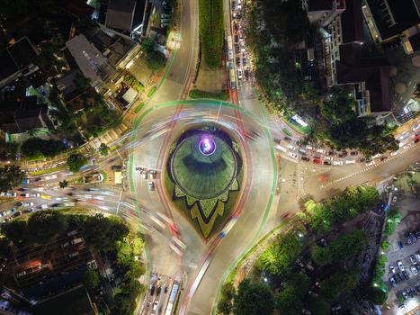 Aerial view of Patung Pemuda Membangun roundabout at night with vibrant traffic light trails surrounding urban greenery and city roads in Kebayoran Baru Jakarta Indonesia. Aerial view of Patung Pemuda Membangun roundabout at night with vibrant traffic light trails surrounding urban greenery and city roads in Kebayoran Baru Jakarta Indonesia.