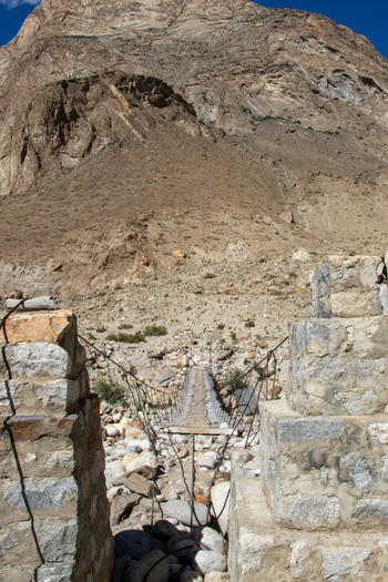 View of a suspension bridge spanning a rocky riverbed with rugged mountain slopes in the background in Gilgit Pakistan. View of a suspension bridge spanning a rocky riverbed with rugged mountain slopes in the background in Gilgit Pakistan.
