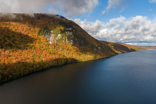 Aerial view of Lake Willoughby with vibrant autumn foliage on surrounding mountains steep cliffs and deep blue water under a partly cloudy sky in Westmore Vermont United States. Aerial view of Lake Willoughby with vibrant autumn foliage on surrounding mountains steep cliffs and deep blue water under a partly cloudy sky in Westmore Vermont United States.