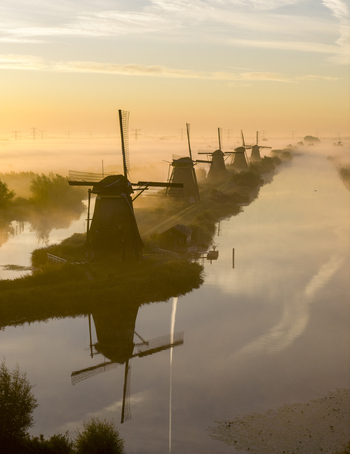 Aerial view of the historic windmills of Kinderdijk shrouded in morning mist with golden reflections on the canal water Kinderdijk Zuid Holland Netherlands.