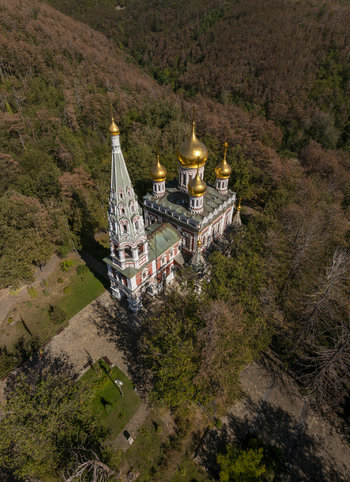 Aerial view of the Shipka Memorial Church with its distinctive golden domes and tall bell tower nestled within a dense forest in Shipka Stara Zagora Bulgaria. Aerial view of the Shipka Memorial Church with its distinctive golden domes and tall bell tower nestled within a dense forest in Shipka Stara Zagora Bulgaria.