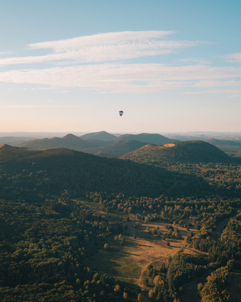 Aerial view of a hot air balloon floating over the volcanic landscape of Puy de Dome in Orcines Auvergne Rhone Alpes France. Aerial view of a hot air balloon floating over the volcanic landscape of Puy de Dome in Orcines Auvergne Rhone Alpes France.